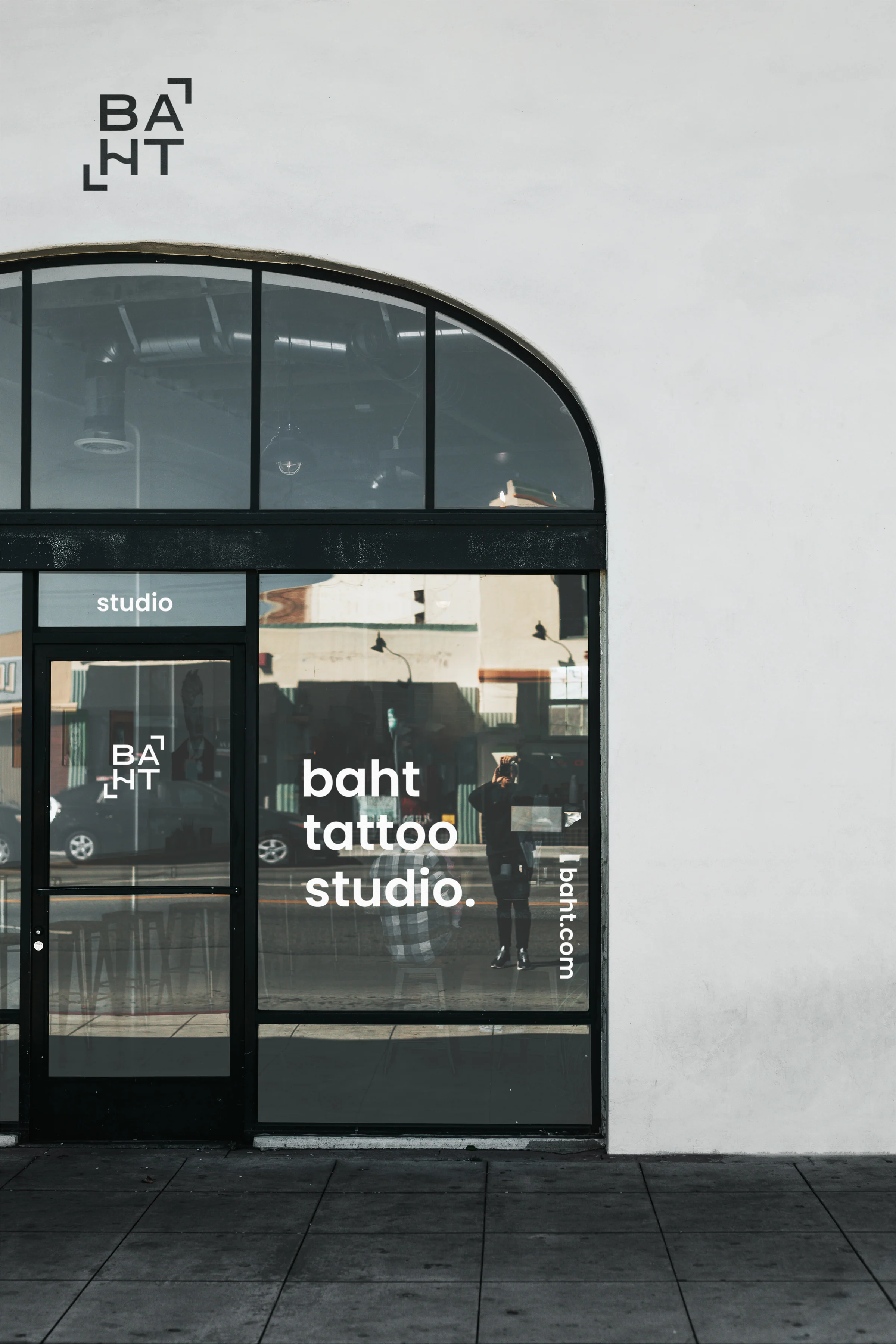 Storefront mockup: baht logo on a white wall above an arched window lettered baht tattoo studio. and baht.com in white.