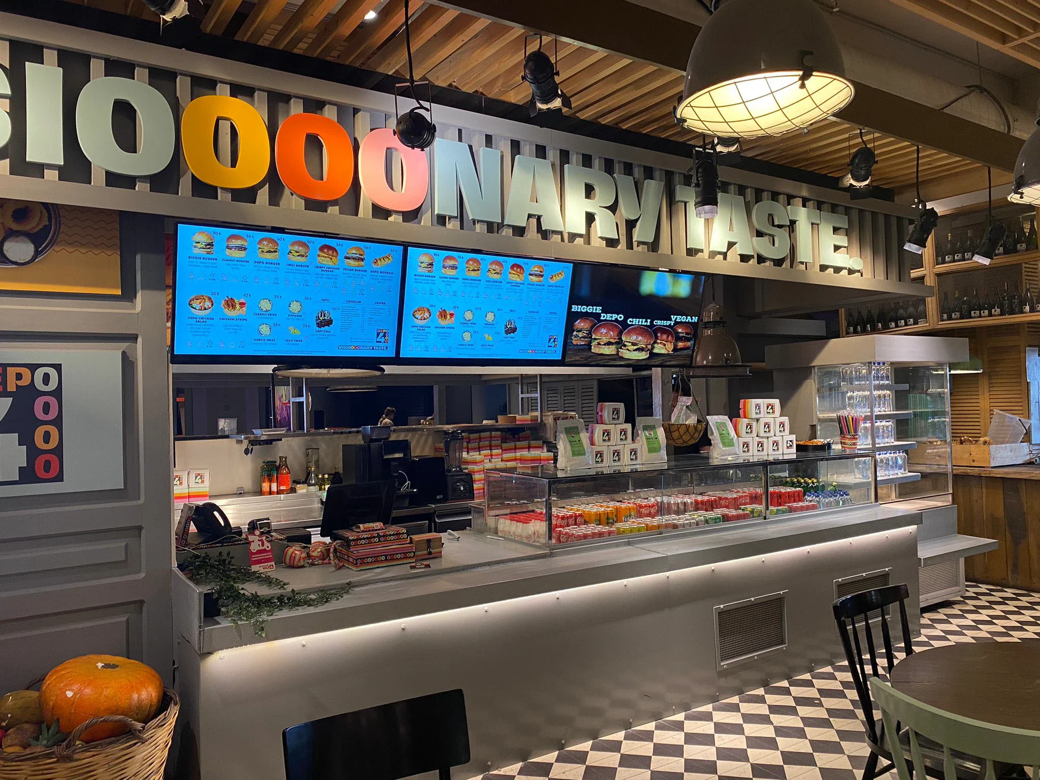 Depo4 counter under Visioooonary Taste lettering, with three menu screens, a logo panel and stacked white boxes on display.