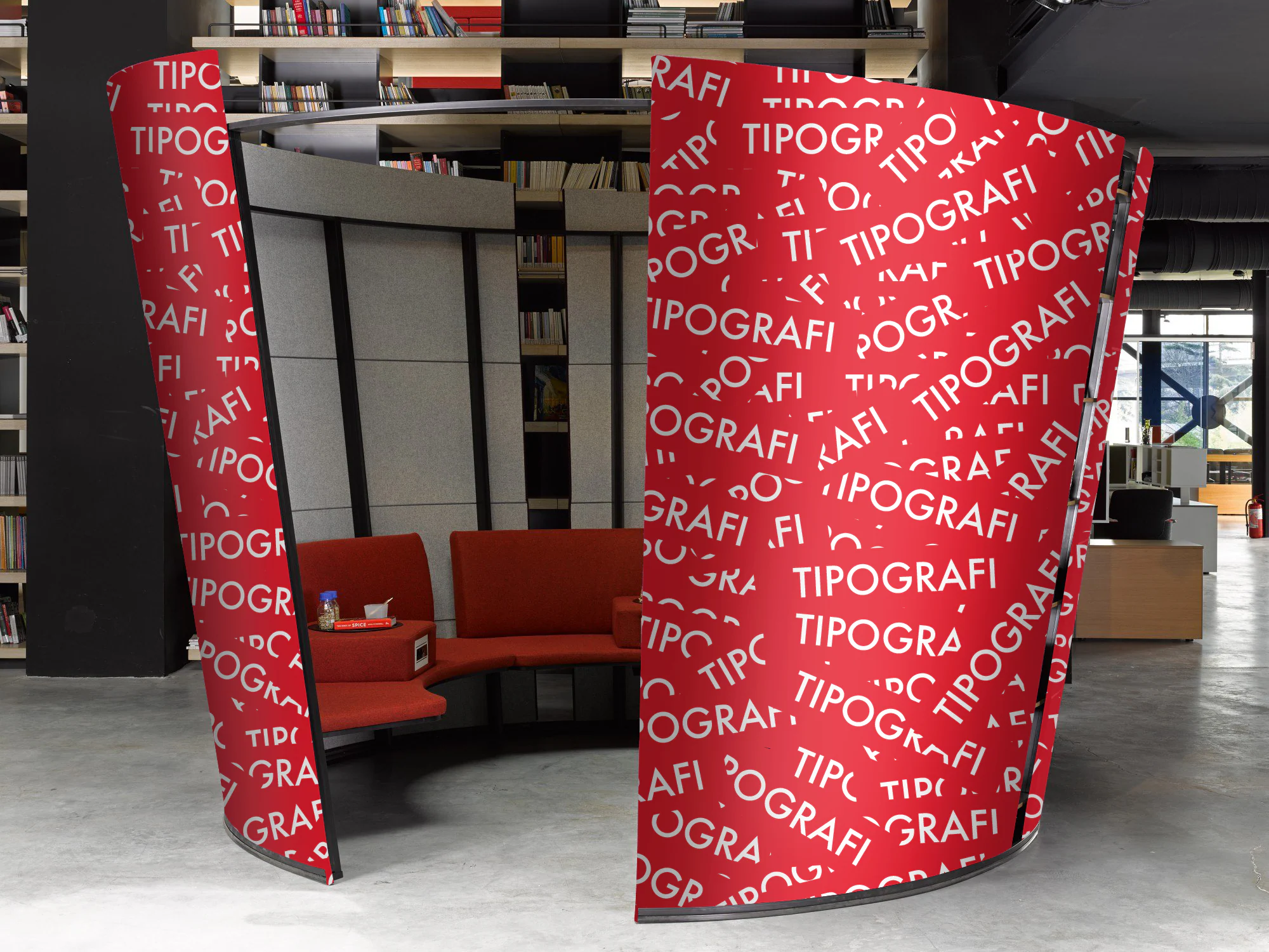 Curved red Oblivion panels wrapped in a white TIPOGRAFI word pattern around a red sofa booth, bookshelves behind.