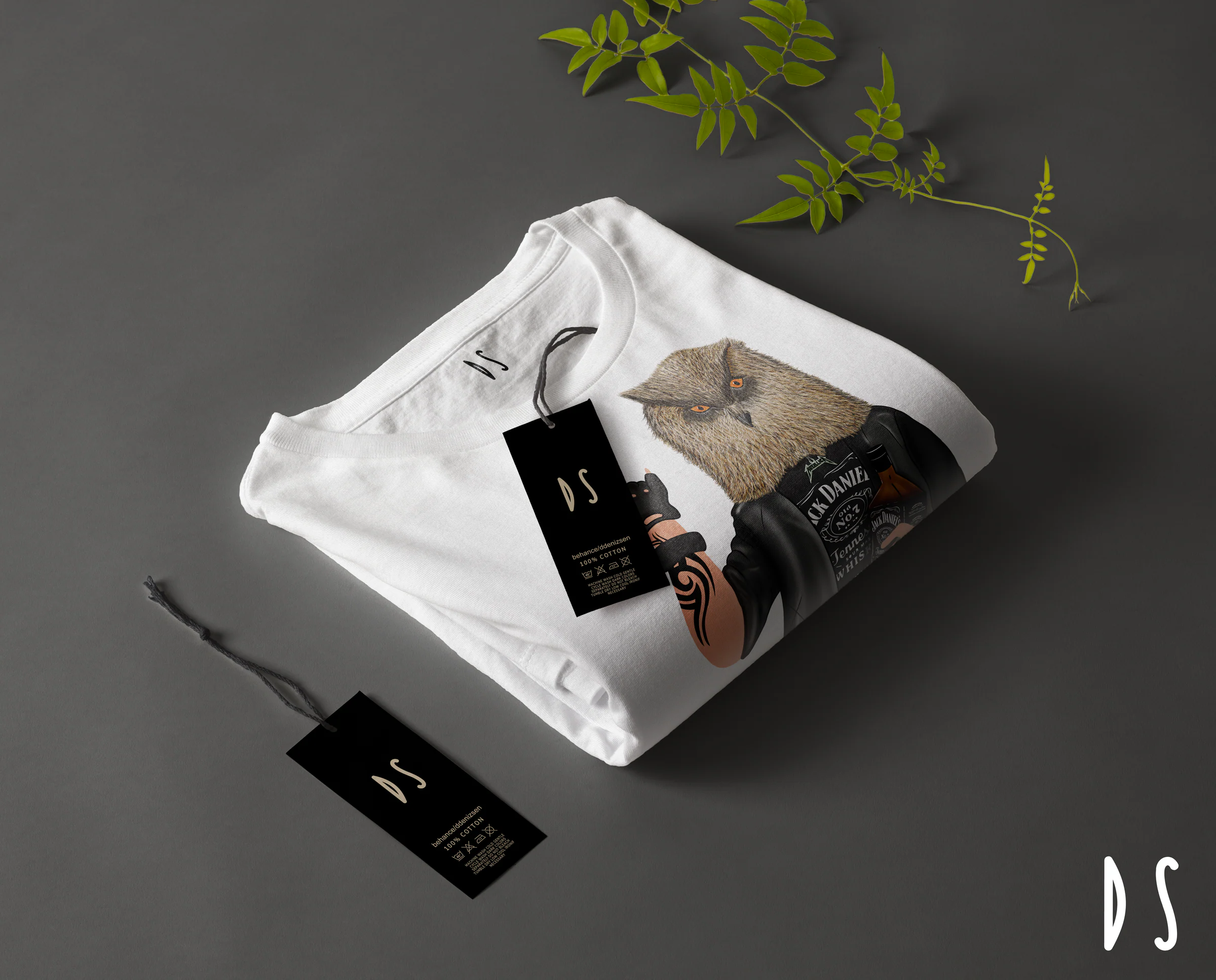 Mockup of a folded white shirt with the punk owl print, a DS neck label and two black DS hang tags on dark grey beside a green sprig.