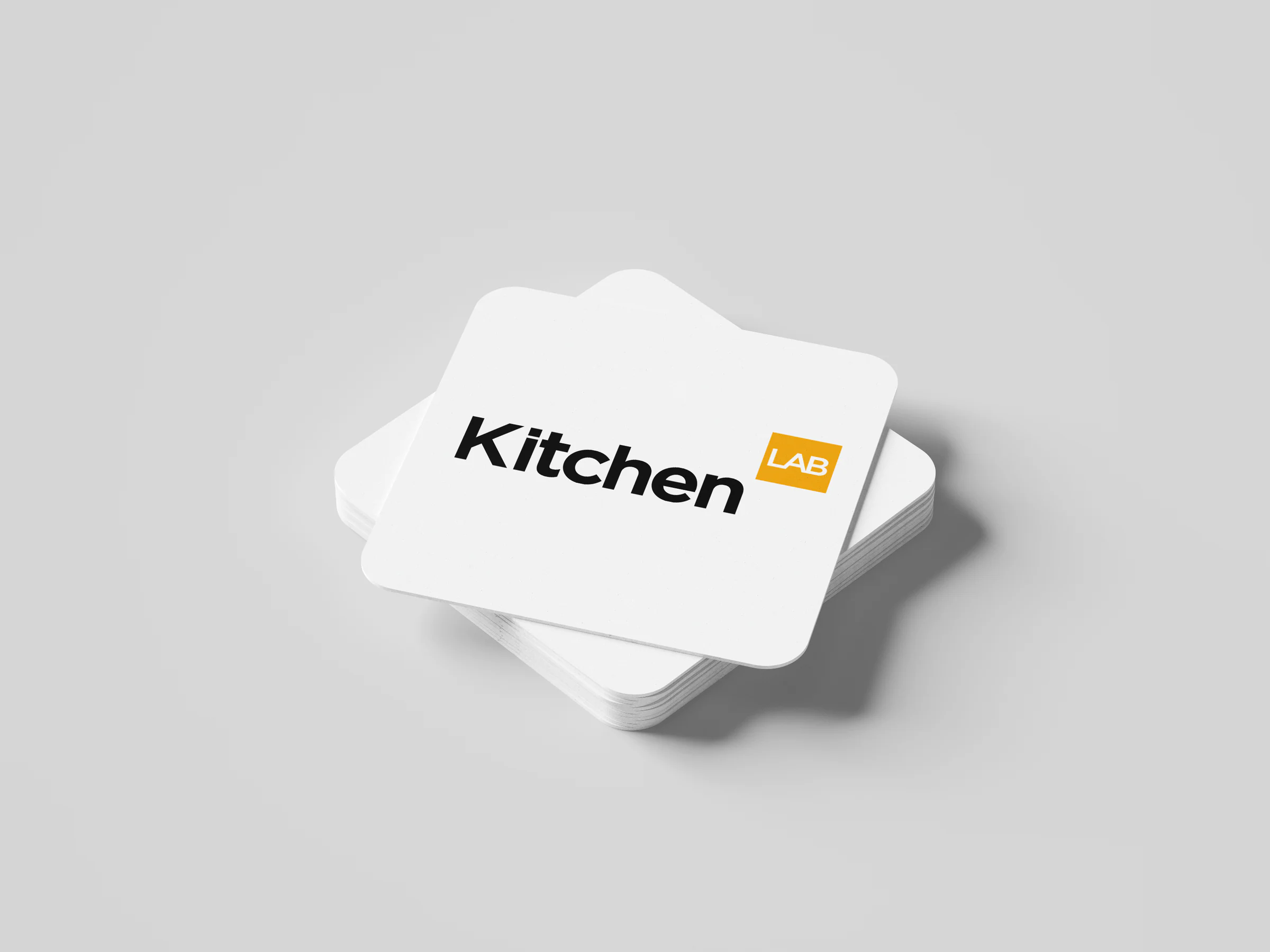 Stack of square white coasters printed with the KitchenLAB logo in black and orange.