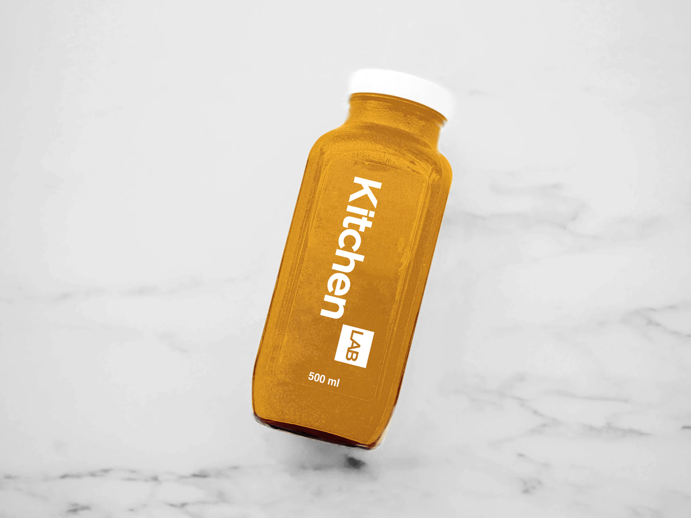 Orange-tinted 500 ml bottle with a white cap and a vertical white KitchenLAB logo, lying on a marble surface.